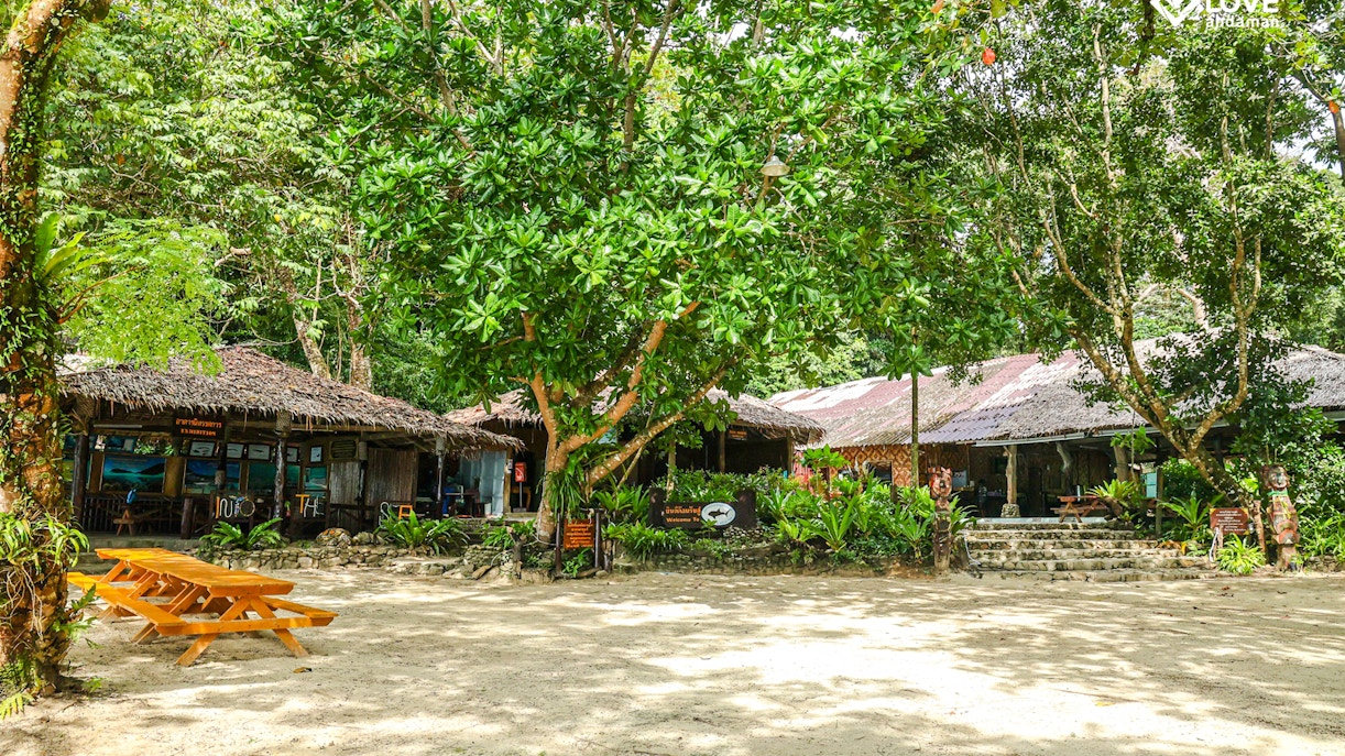Thatched-roof buildings and picnic tables on a sandy clearing in the Surin Islands.
