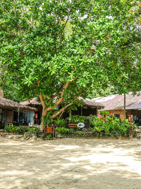 Thatched-roof buildings and picnic tables on a sandy clearing in the Surin Islands.