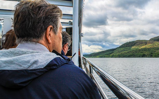 Passengers enjoying scenic views from a cruise on a lake with hills in the background.