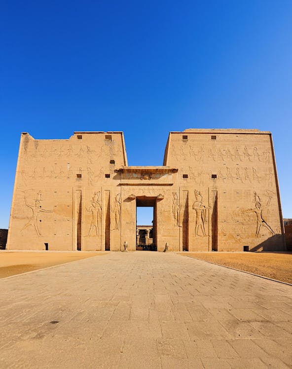 Edfu Temple entrance with ancient Egyptian carvings under a clear blue sky.