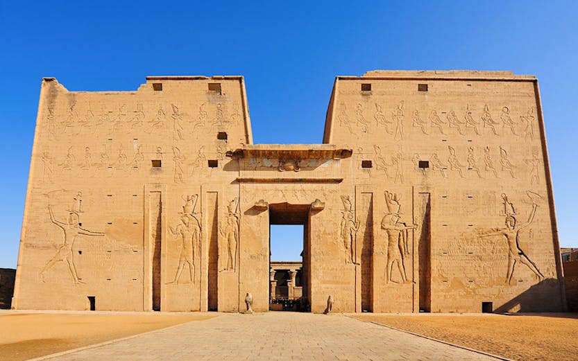 Edfu Temple entrance with ancient Egyptian carvings under a clear blue sky.