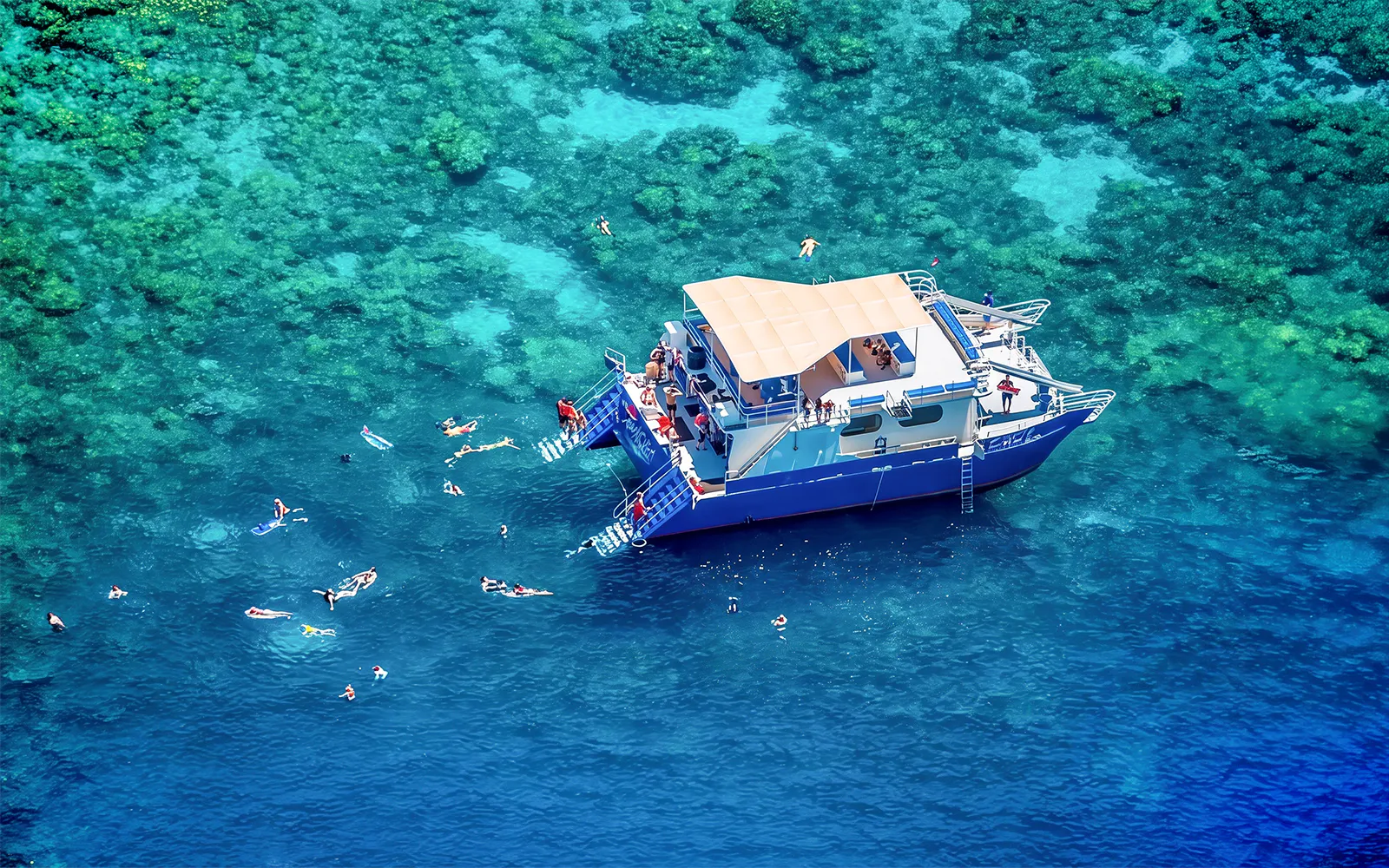 Snorkelers near a boat in Kealakekua Bay, Hawaii, exploring coral reefs.