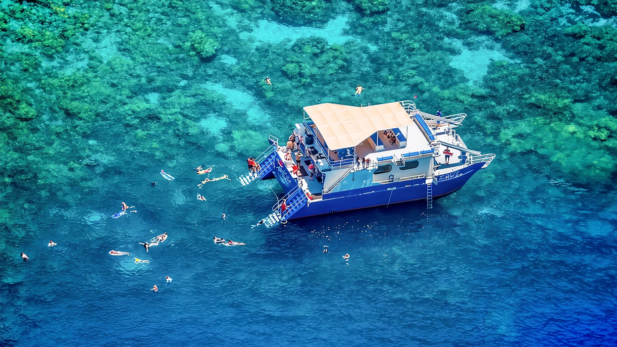 Snorkelers near a boat in Kealakekua Bay, Hawaii, exploring coral reefs.