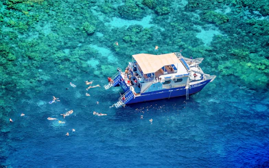 Snorkelers near a boat in Kealakekua Bay, Hawaii, exploring coral reefs.