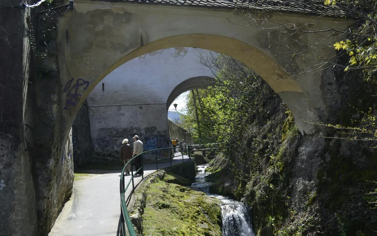 Pathway under stone arches with people walking, part of the Romantic Brasov Lady and the Knight tour, Brasov.