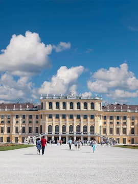 Visitors walking towards Schönbrunn Palace in Vienna under a blue sky.