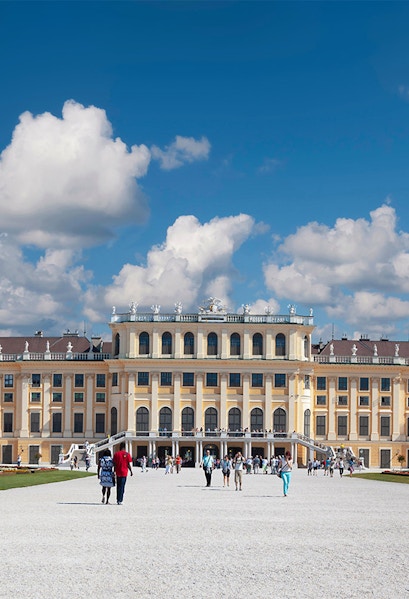 Visitors walking towards Schönbrunn Palace in Vienna under a blue sky.