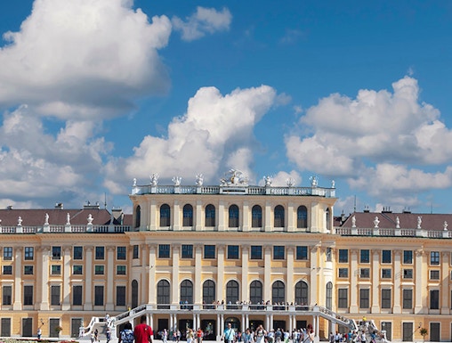 Visitors walking towards Schönbrunn Palace in Vienna under a blue sky.