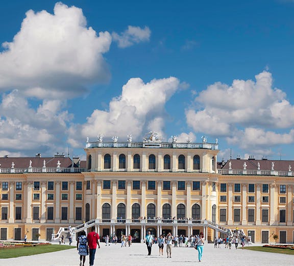 Visitors walking towards Schönbrunn Palace in Vienna under a blue sky.