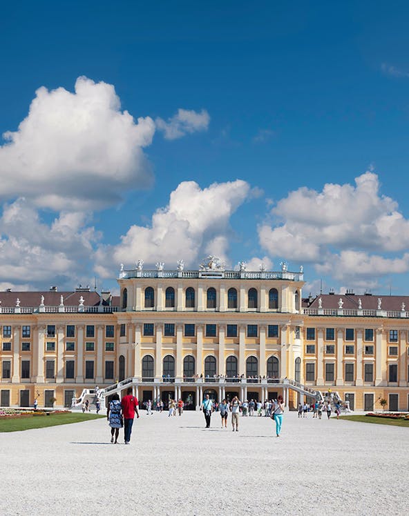 Visitors walking towards Schönbrunn Palace in Vienna under a blue sky.