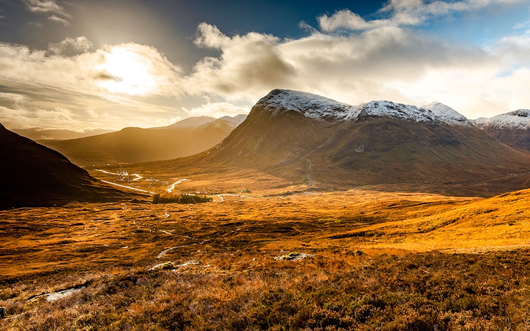Glencoe valley with sunlit mountains and a winding river in Scotland.