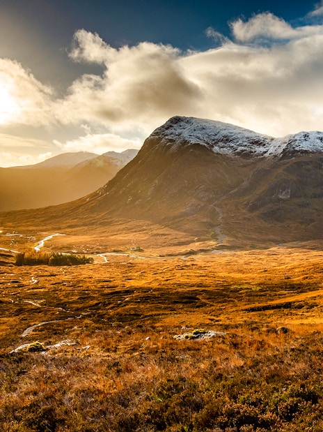 Glencoe valley with sunlit mountains and a winding river in Scotland.