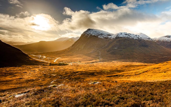 Glencoe valley with sunlit mountains and a winding river in Scotland.