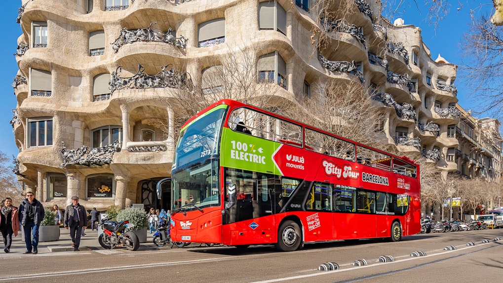 Barcelona hop-on hop-off bus in front of Casa Milà, Gaudí's architectural landmark.