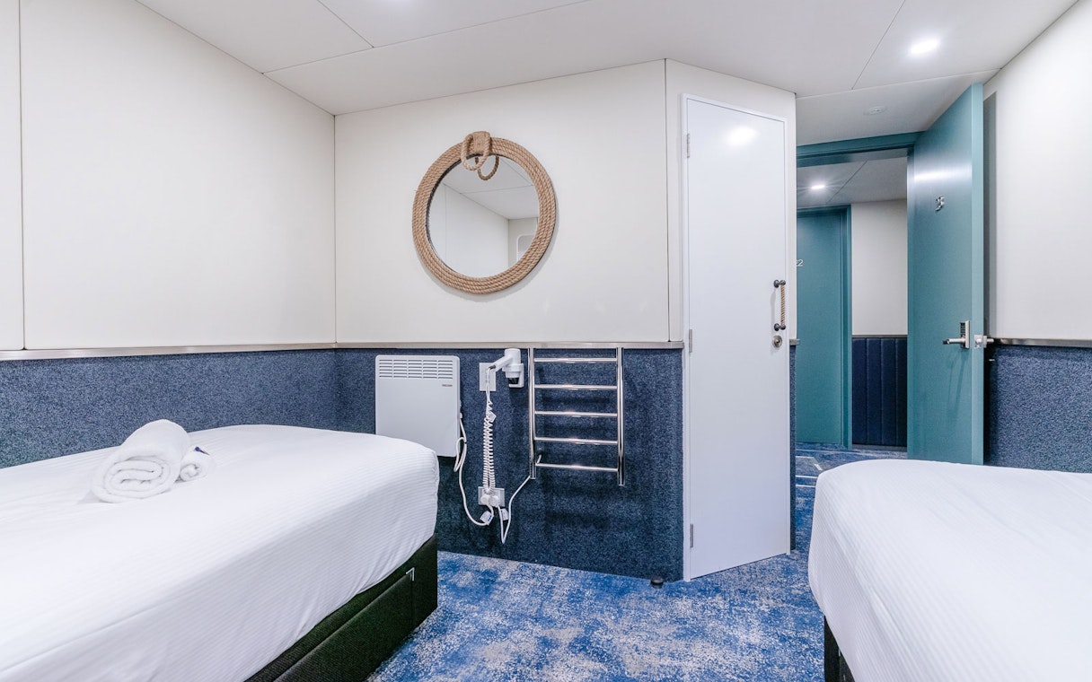 Cruise ship cabin interior with twin beds and nautical decor.