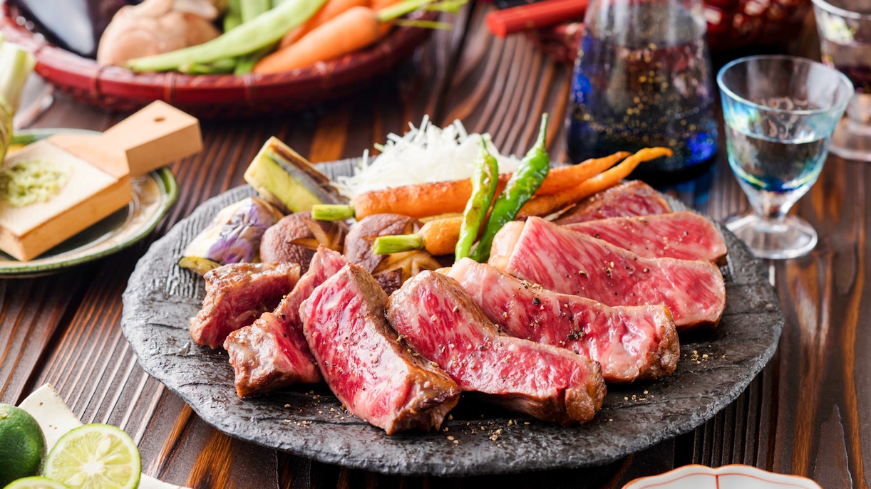 Wagyu steak served with grilled vegetables on a stone plate.