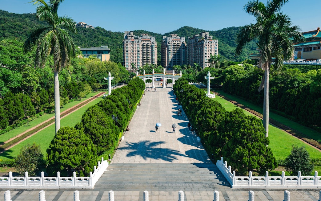 Walkway leading to Taiwan Palace Museum with lush greenery and distant buildings.