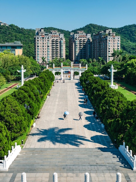 Walkway leading to Taiwan Palace Museum with lush greenery and distant buildings.