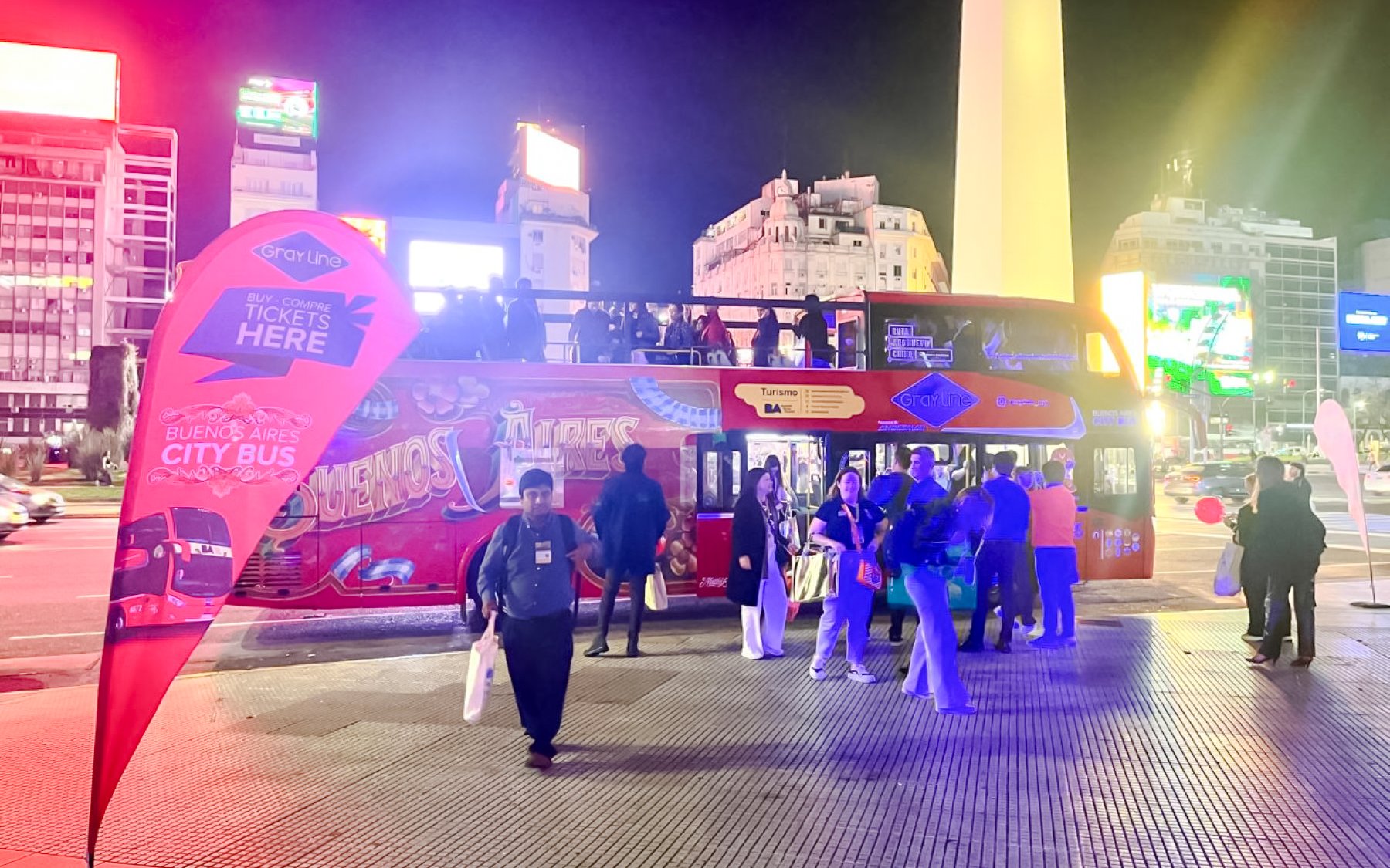 Open-top bus at night in Buenos Aires with tourists boarding near the Obelisk.