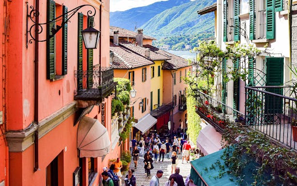 Colorful street in Bellagio, Italy, with tourists exploring shops and cafes, part of Como city and Bellagio tour.