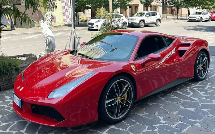 Red Ferrari 488 parked on a cobblestone street with a statue in the background.