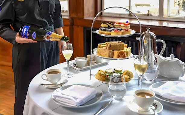 Server pouring champagne for afternoon tea with sandwiches and pastries at the London Eye.