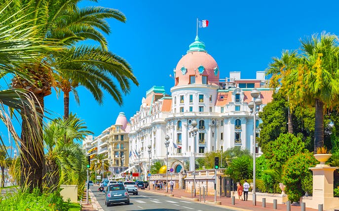 Walking tour in Nice's Old Town with view of iconic hotel and palm-lined street.