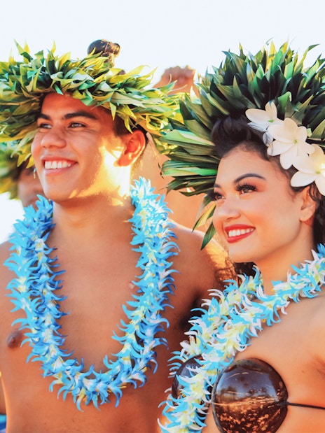 Performers in traditional attire at Moana Luau, Hawaii, wearing floral leis and headpieces.