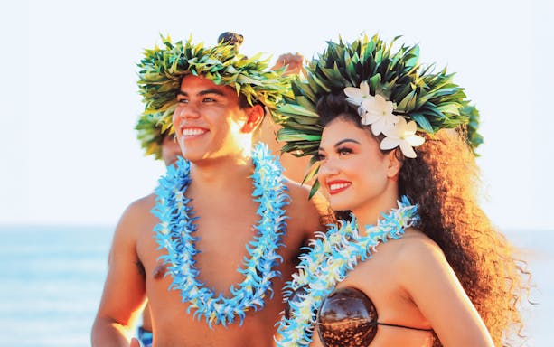 Performers in traditional attire at Moana Luau, Hawaii, wearing floral leis and headpieces.