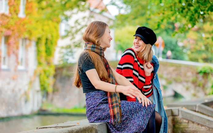 Two people sitting on a canal bridge in Bruges, surrounded by greenery.