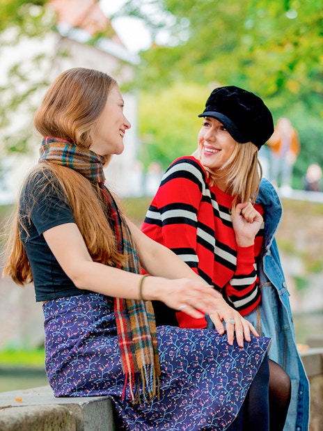 Two people sitting on a canal bridge in Bruges, surrounded by greenery.