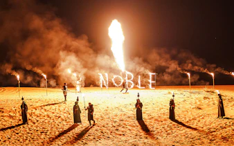 Fire performance at Noble Camp Desert Safari with torches and "Noble" in flames.