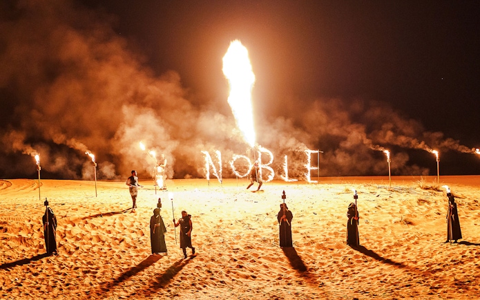 Fire performance at Noble Camp Desert Safari with torches and "Noble" in flames.