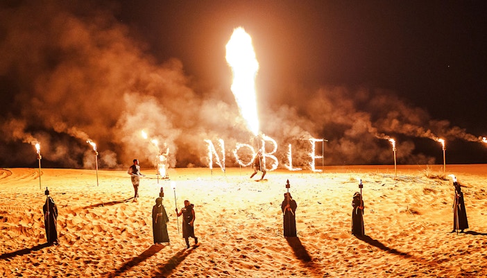 Fire performance at Noble Camp Desert Safari with torches and "Noble" in flames.