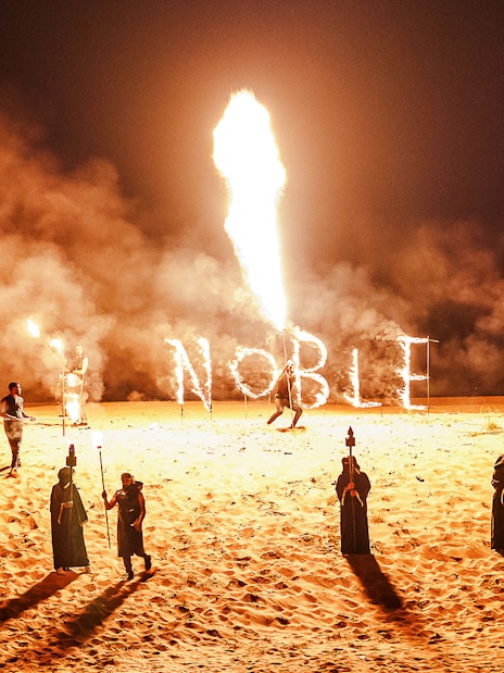 Fire performance at Noble Camp Desert Safari with torches and "Noble" in flames.