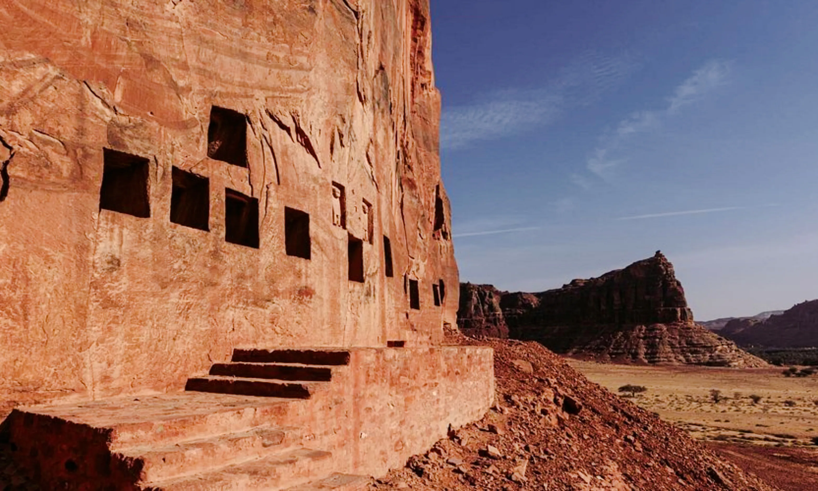 Ancient rock-cut tombs at Hegra, AlUla, with desert landscape in the background.