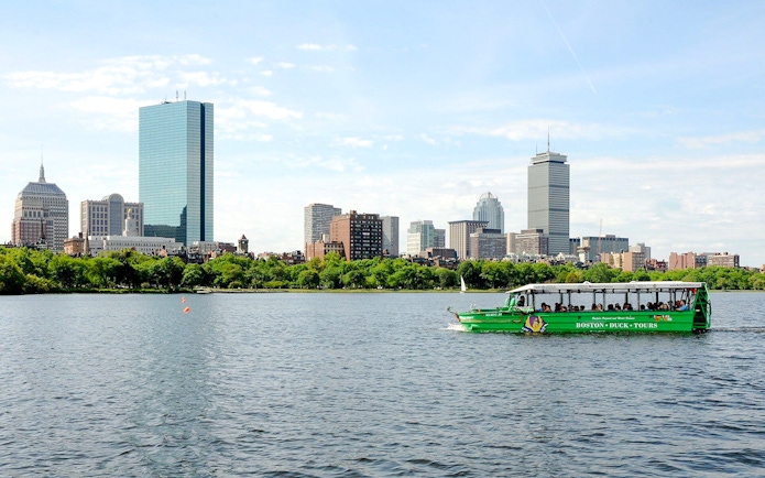 Boston Duck Tours vehicle cruising on Charles River with Boston skyline in background.