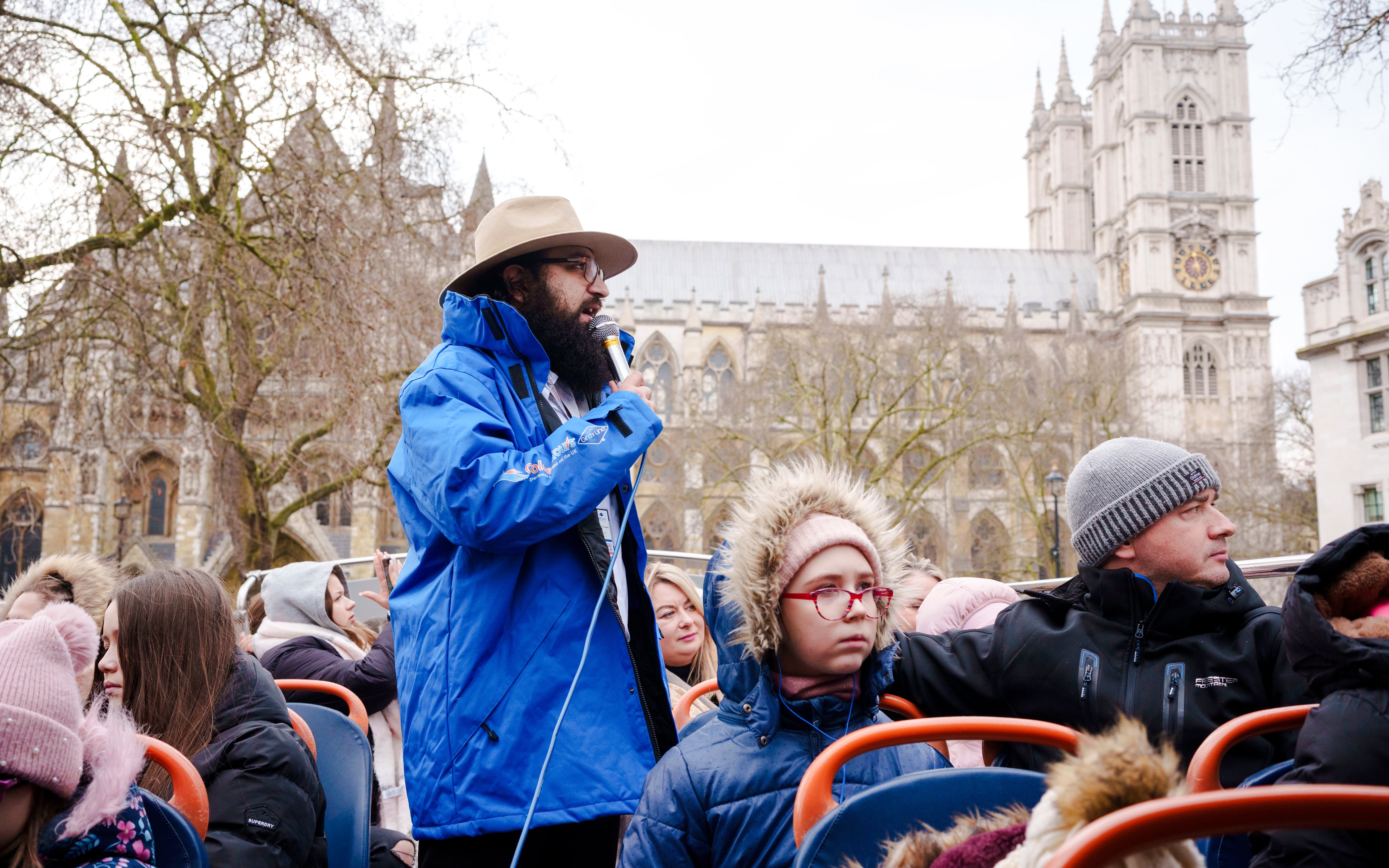 Tour guide speaking on a Golden Tours hop-on hop-off bus near Westminster Abbey, London.