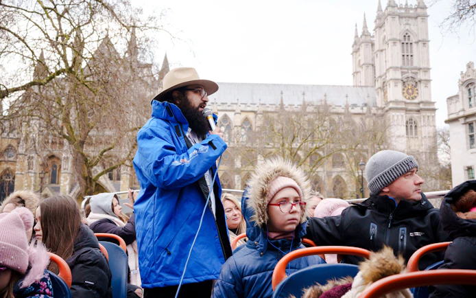 Tour guide speaking on a Golden Tours hop-on hop-off bus near Westminster Abbey, London.