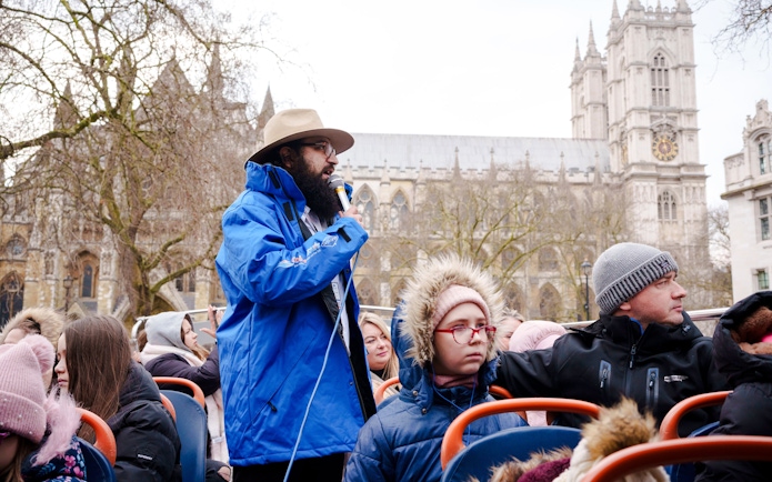 Tour guide speaking on a Golden Tours hop-on hop-off bus near Westminster Abbey, London.