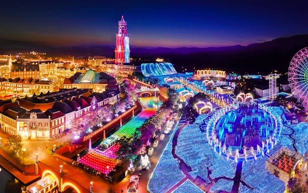 Huis Ten Bosch illuminated at night with colorful lights and Ferris wheel, seen on a 1-day bus tour from Fukuoka Airport.