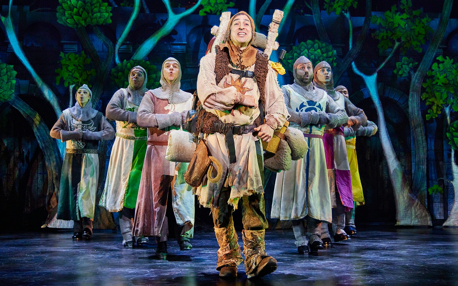 Actors in medieval costumes performing a scene from Spamalot on stage.