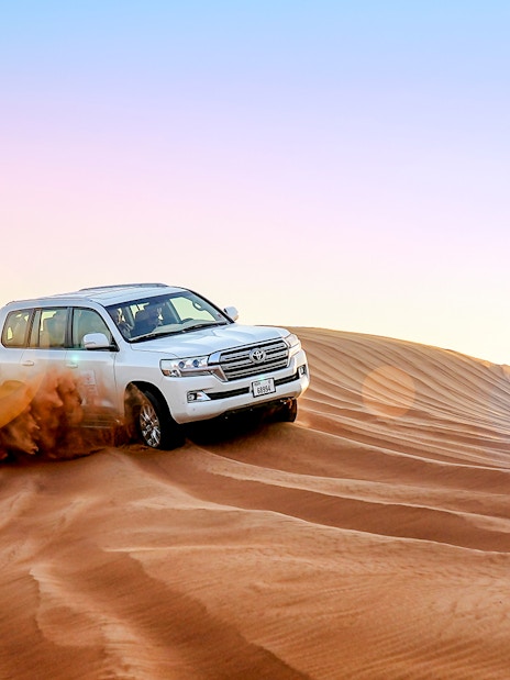 SUV driving over sand dunes during evening desert safari.