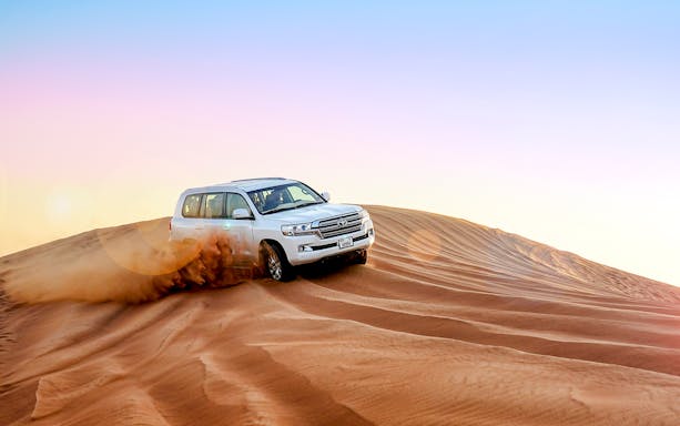 SUV driving over sand dunes during evening desert safari.