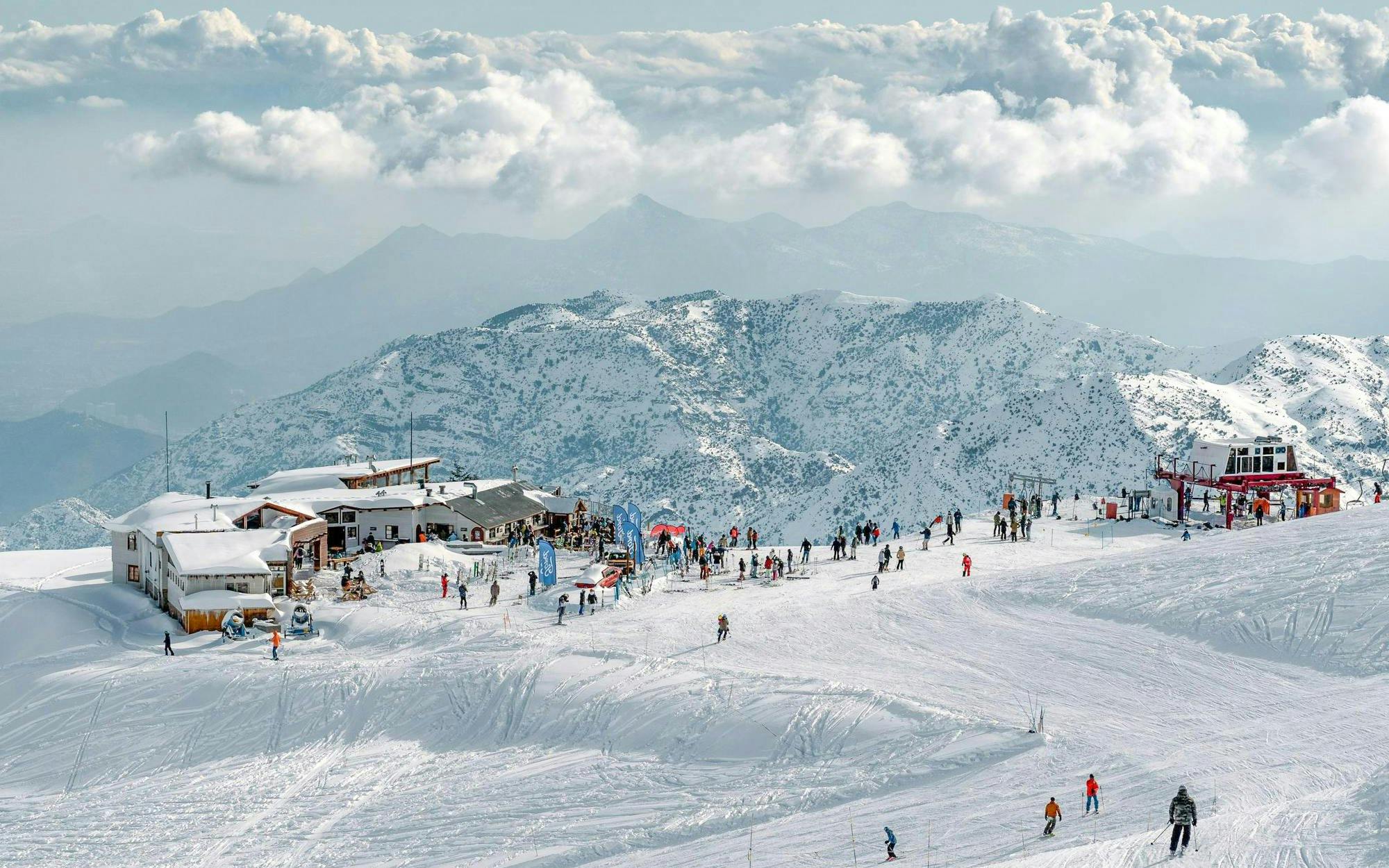 Skiers enjoying slopes at Farellones Ski resort with snowy Andes mountains in the background.