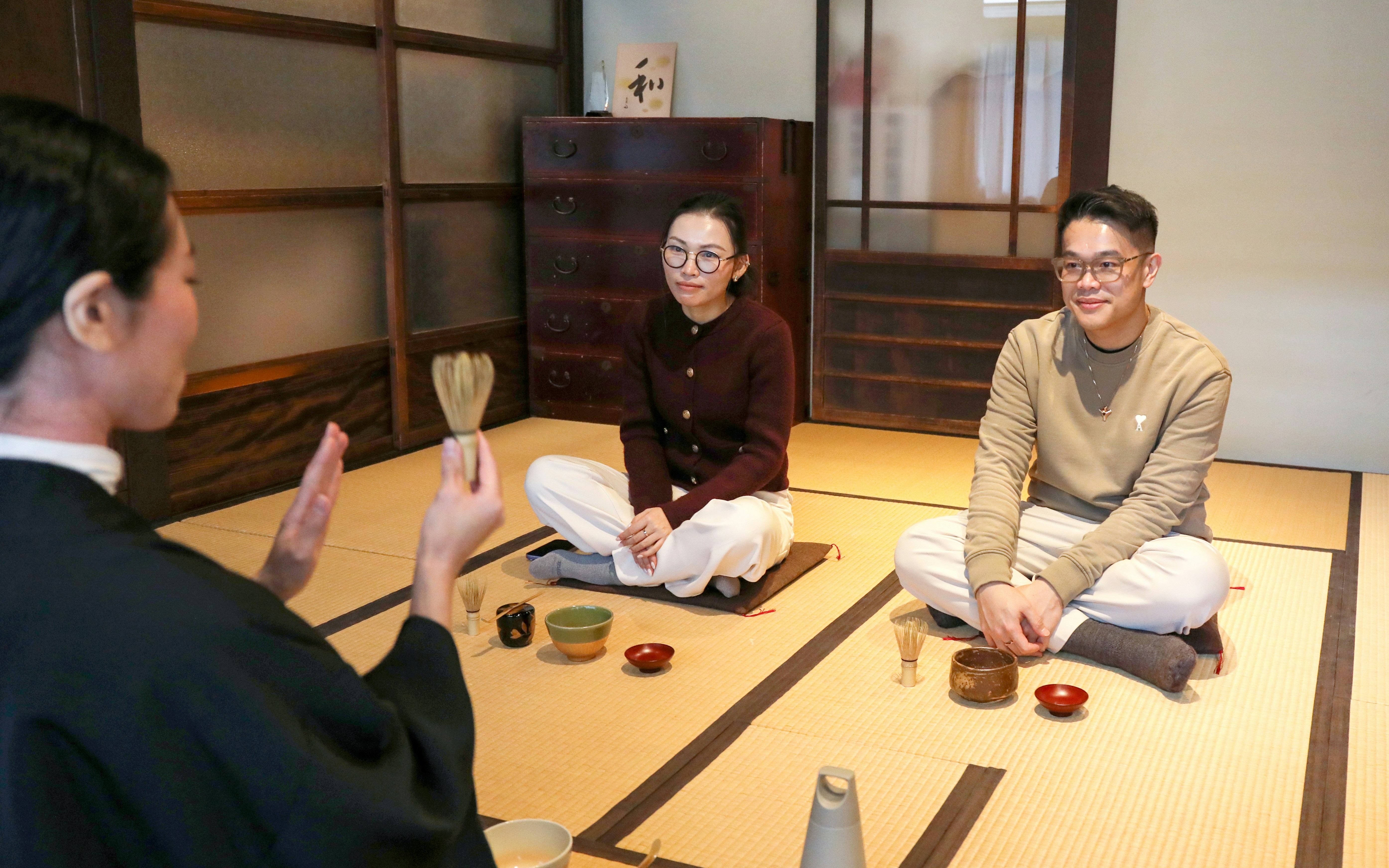 Guide demonstrating tea-making process to seated participants in a traditional Japanese room.