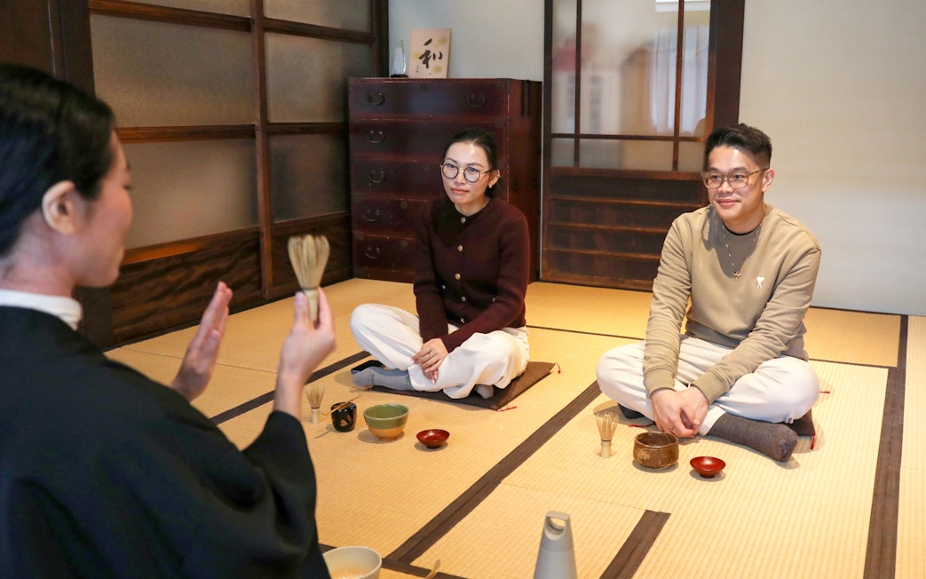 Guide demonstrating tea-making process to seated participants in a traditional Japanese room.