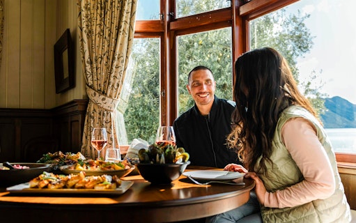Couple enjoying a meal at Walter Peak Gourmet BBQ Experience with lake view.