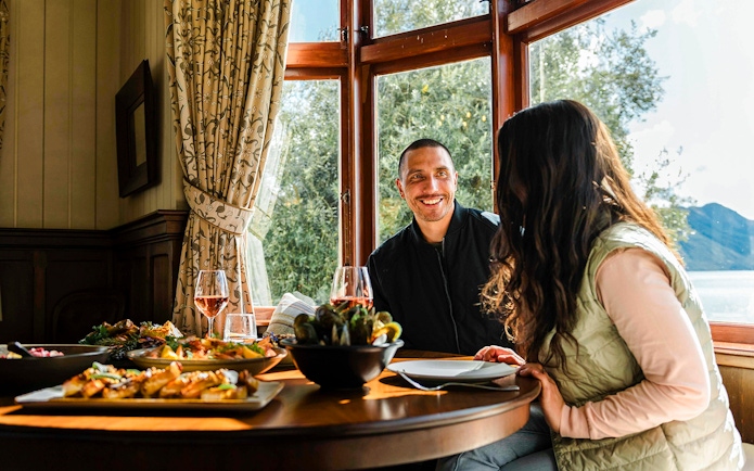 Couple enjoying a meal at Walter Peak Gourmet BBQ Experience with lake view.
