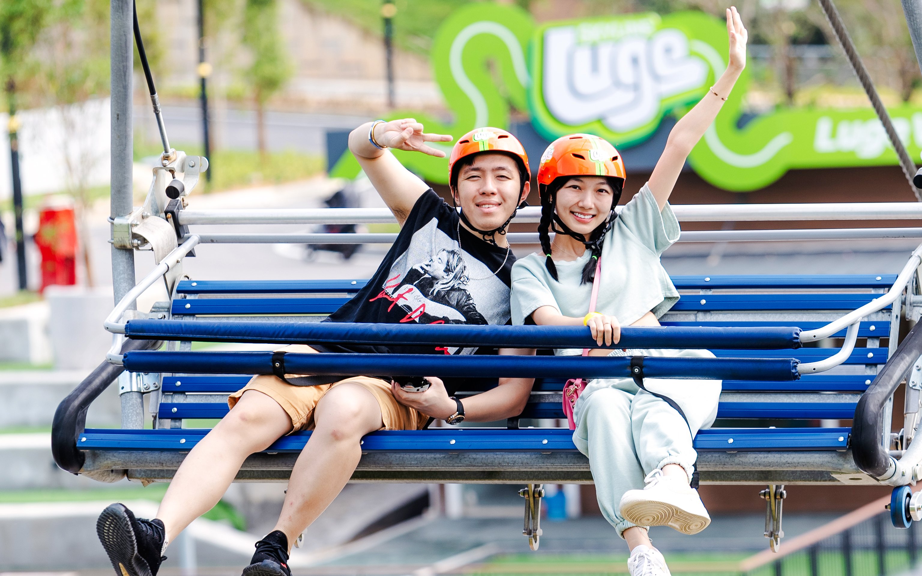 Couple on chairlift at Skyline Luge Kuala Lumpur, wearing helmets and smiling.